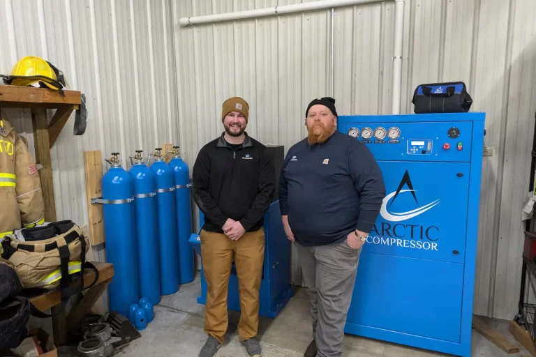 Two men in work attire standing next to Arctic Compressor 1500 Series and air cylinders in a workshop.